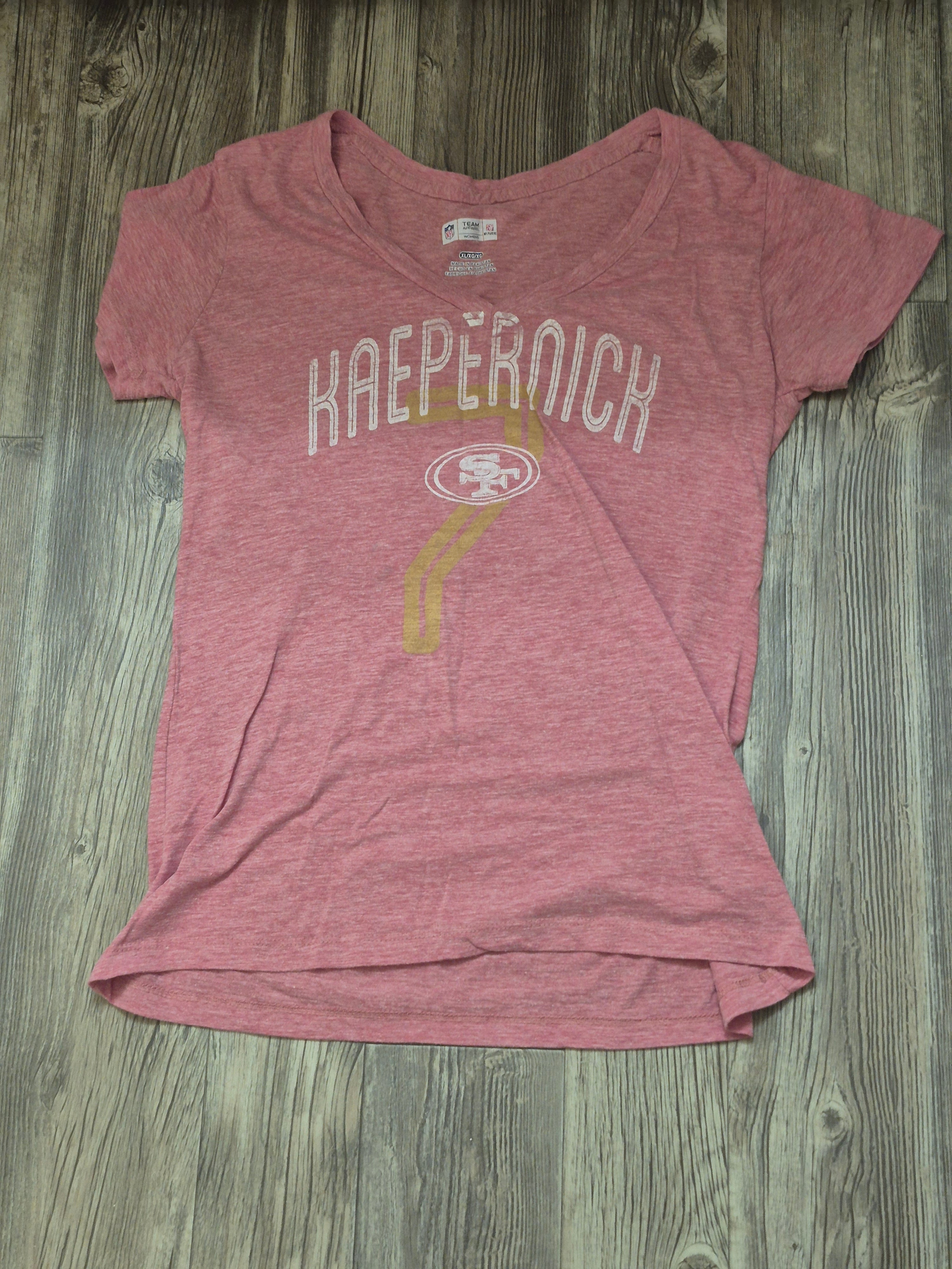 Pink t-shirt with 'Kaepernick' printed on it, lying flat on a wooden surface