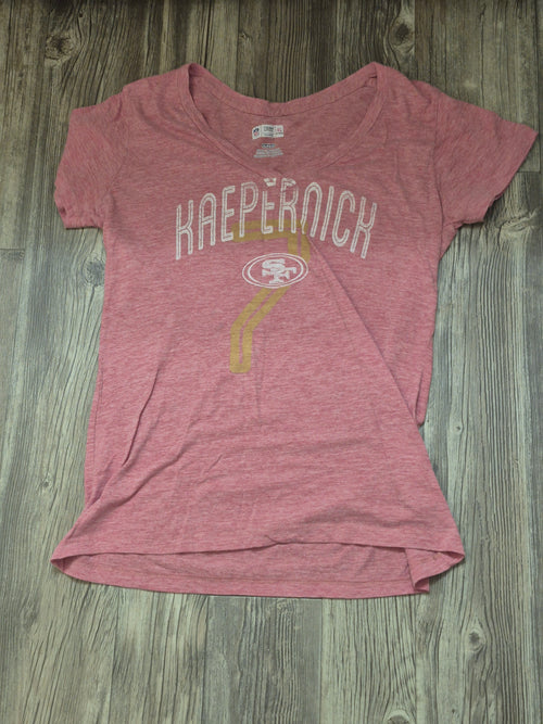 Pink t-shirt with 'Kaepernick' printed on it, lying flat on a wooden surface